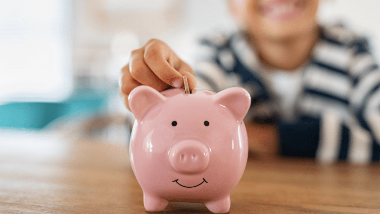 menino colocando uma moeda em um cofrinho com o formato de um porquinho cor de rosa