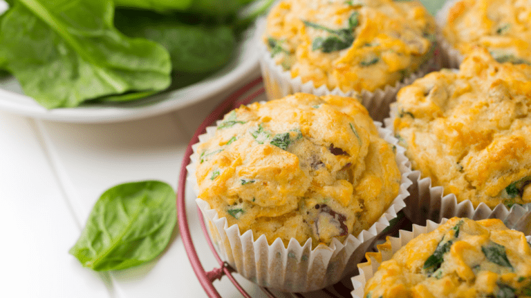 imagem mostra alguns muffins de espinafre, em uma mesa de madeira ao lado de uma tigela com folhas frescas de espinafre